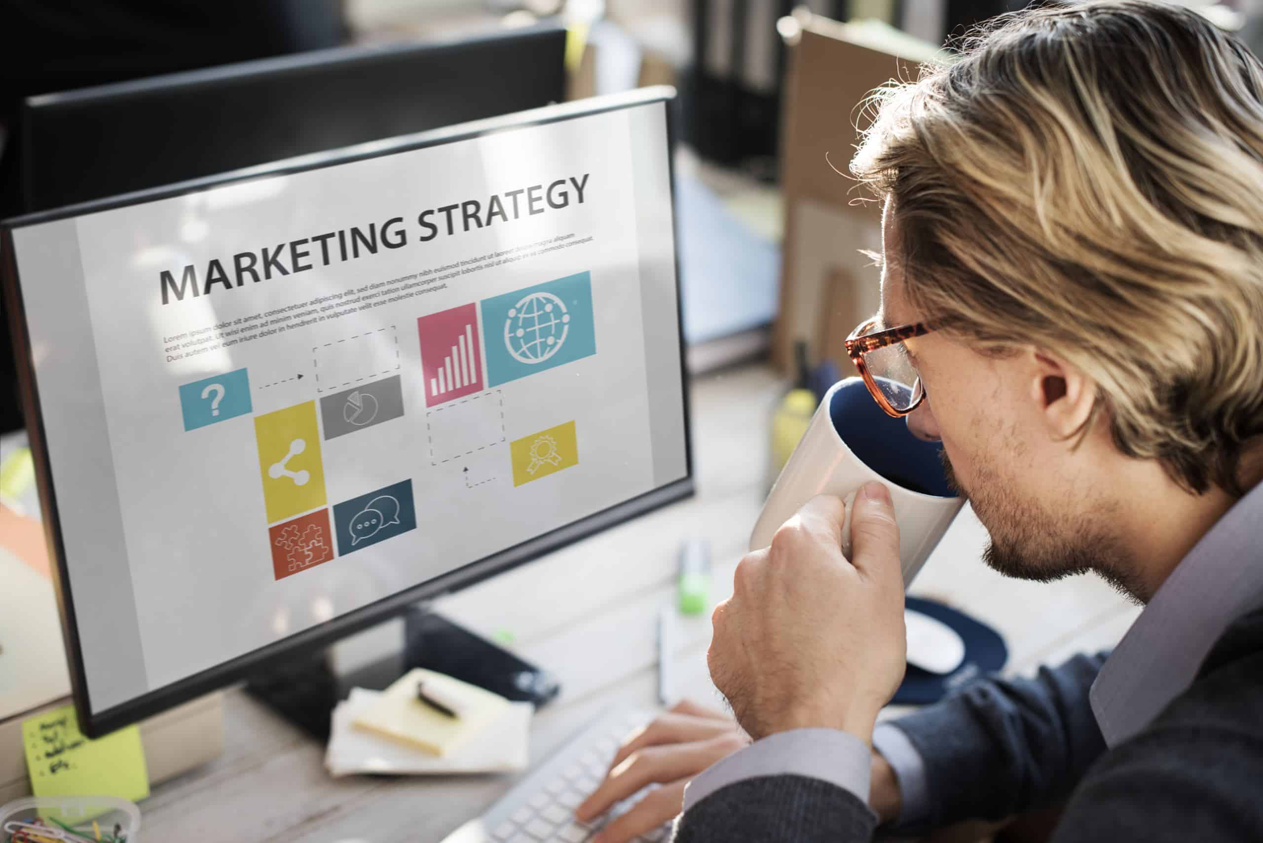 closeup caucasian man drinking coffee with computer screen showing marketing strategy scaled
